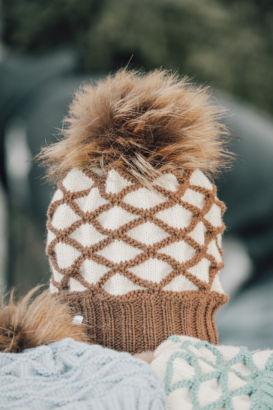 A knitted hat with a diamond pattern and a fur pompom.