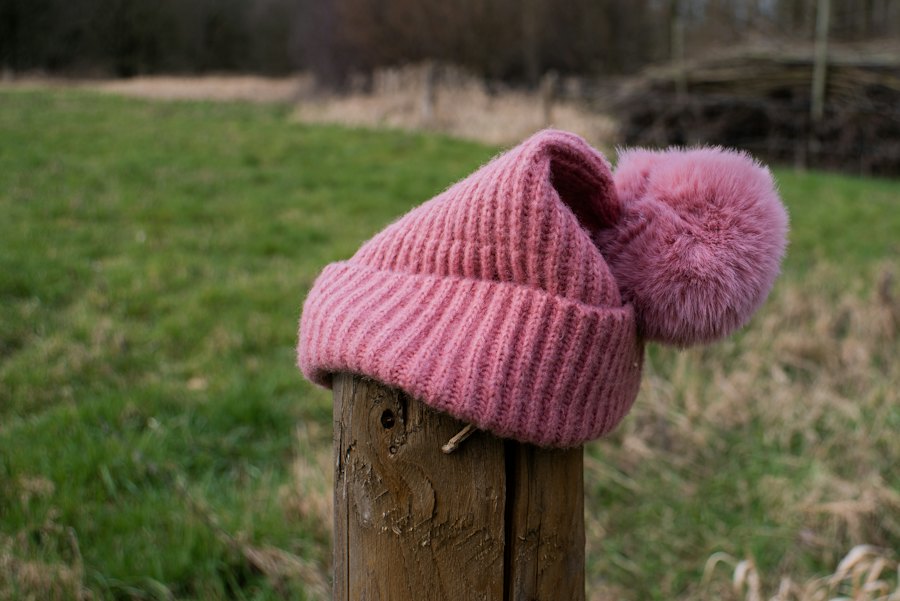A pink ribbed hat with a pompom on a fence post.