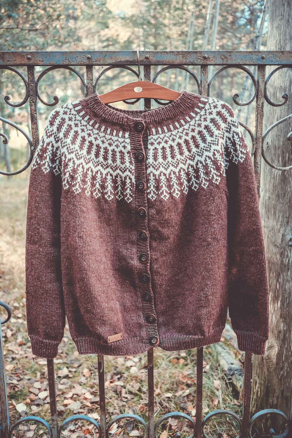 A brown cardigan with a cream Nordic yoke hanging on an iron gate.