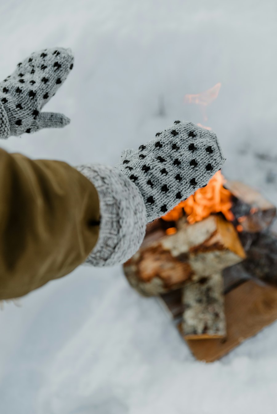 Grey knitted mittens with a dotted pattern held out in the snow.