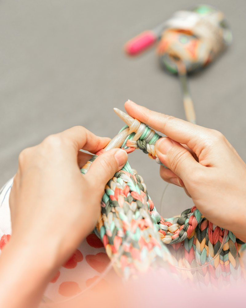 Hands knitting a colourful piece on needles.