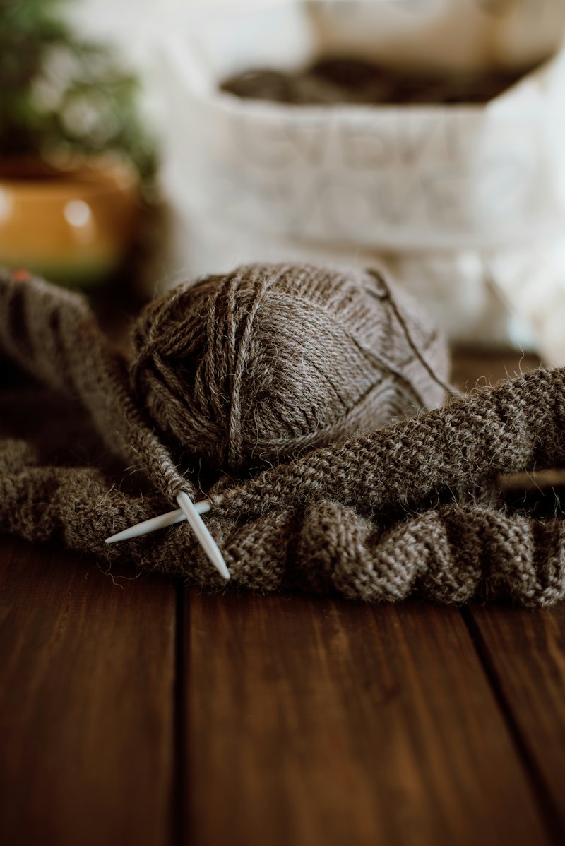 A knitted piece on a dark wooden table with scissors and yarn.