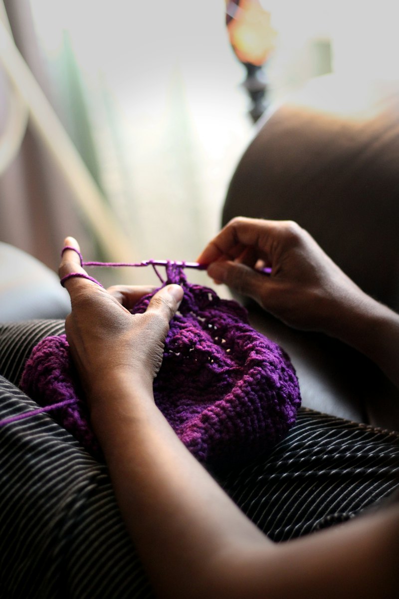 Hands crocheting a purple piece.