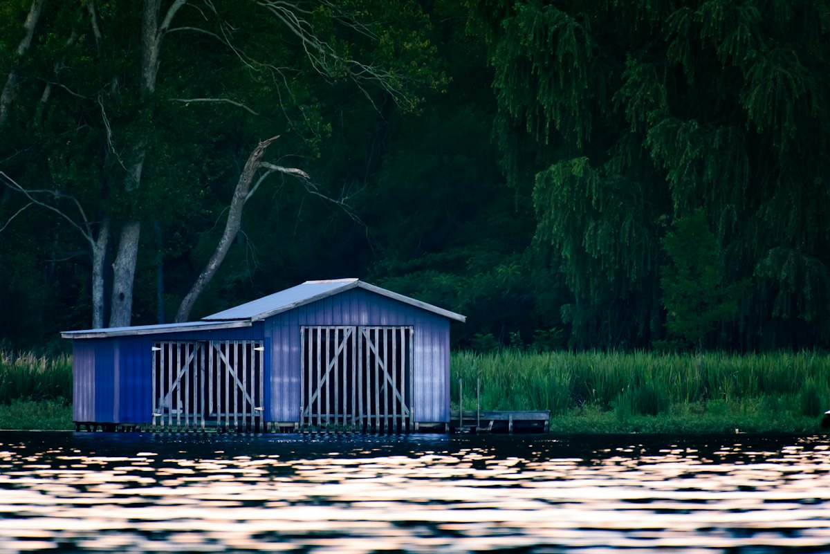 A blue wooden boathouse at the water's edge.