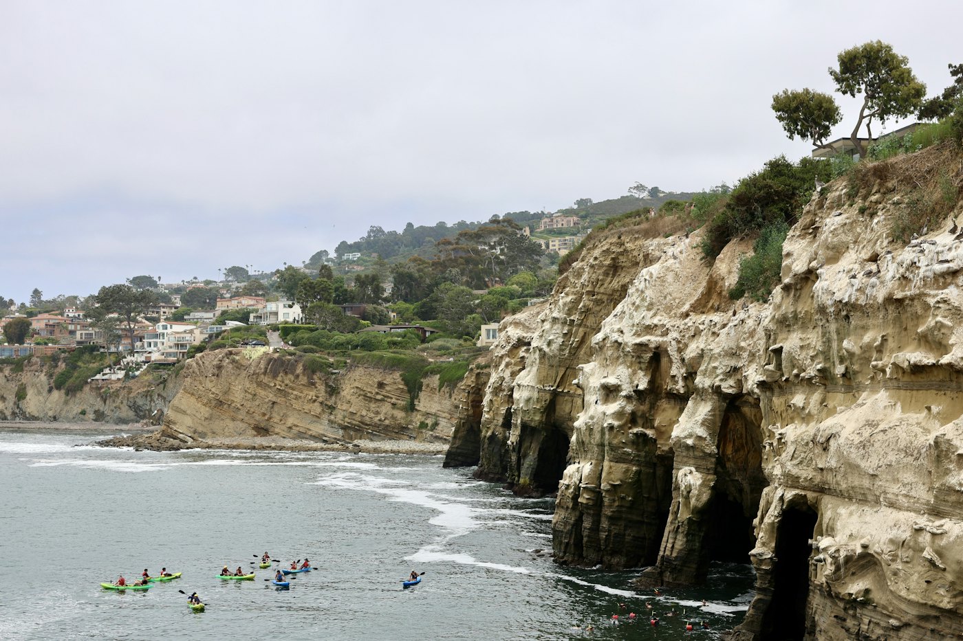 A line of paddlers on the sea beneath coastal cliffs.